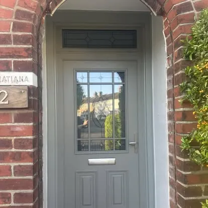 Sage green composite front door with a glazed panel in a red brick porch