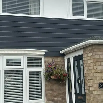 Dark grey cladding above white bay windows and a black front door