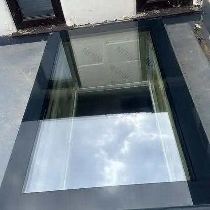 Dark-framed flat roof skylight seen from above, reflecting clouds